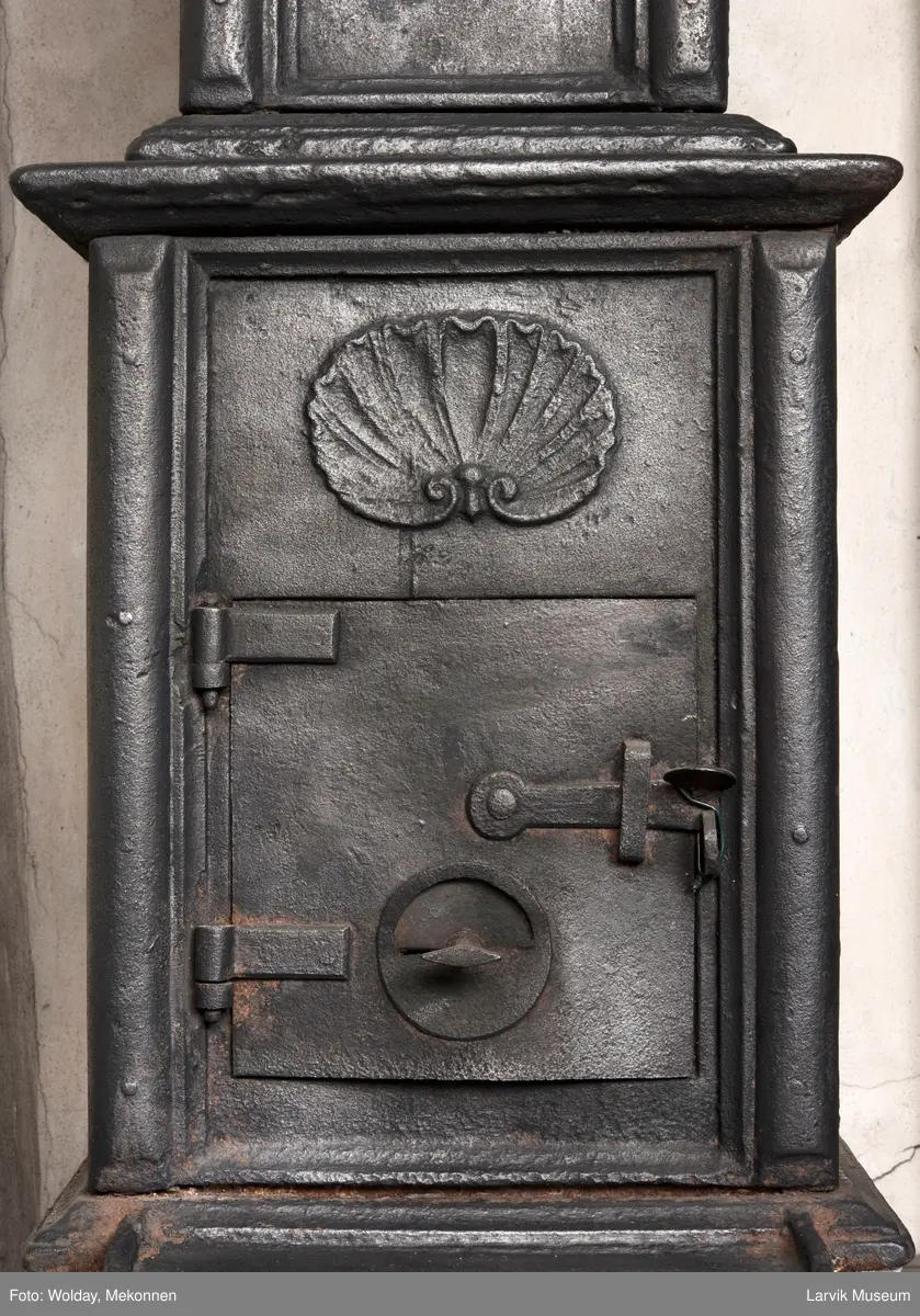 Jernovn med to etasjer, begge er rektangulære. Ovn står på muret fot/understell.
1etasje langside: Vulkan som smed .
1etasje kortside: Musling. 
2etasje langside: Buet åpning i profilert innramming omgitt av girlander. 
2etasje kortside: Overflødighetshorn.