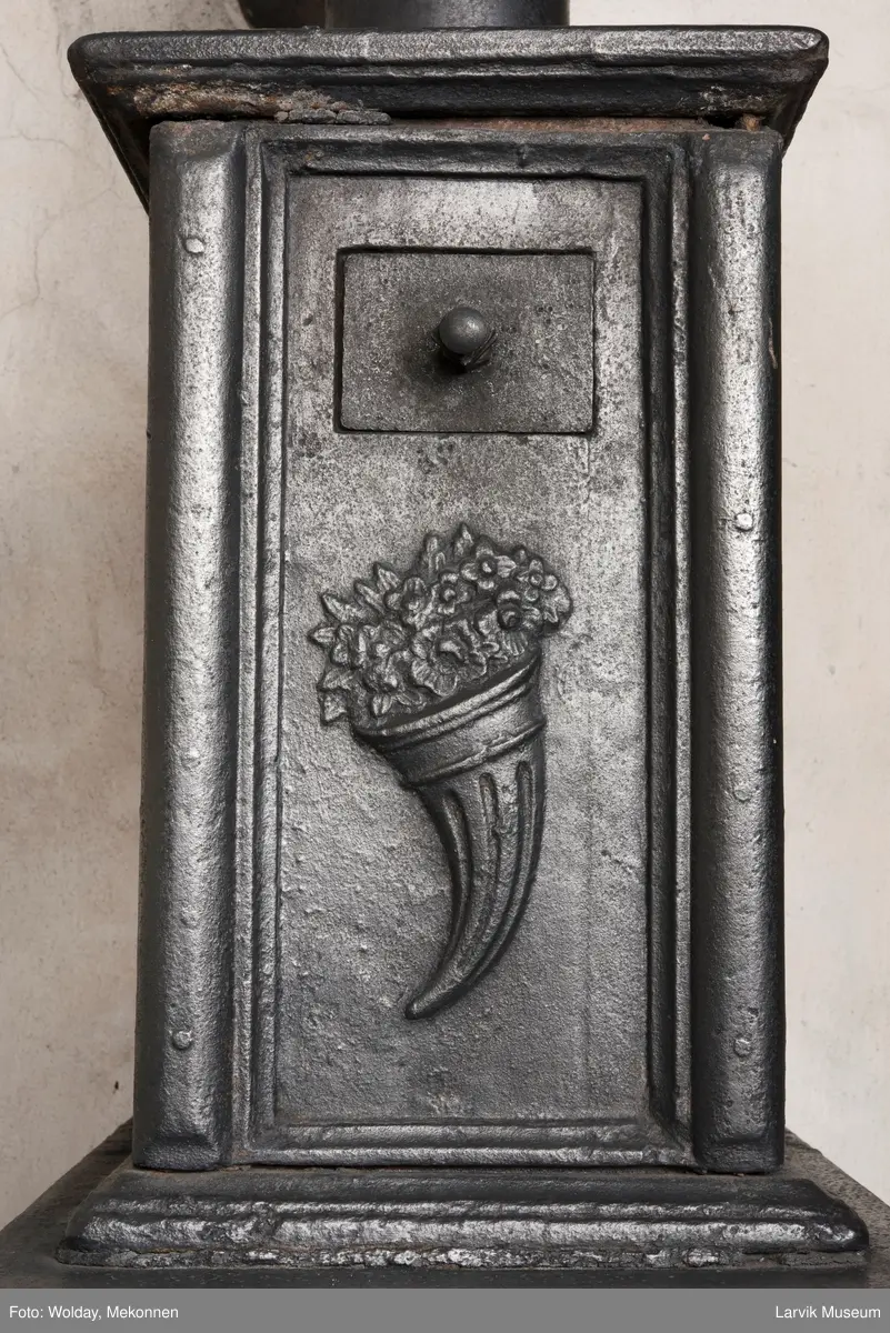 Jernovn med to etasjer, begge er rektangulære. Ovn står på muret fot/understell.
1etasje langside: Vulkan som smed .
1etasje kortside: Musling. 
2etasje langside: Buet åpning i profilert innramming omgitt av girlander. 
2etasje kortside: Overflødighetshorn.