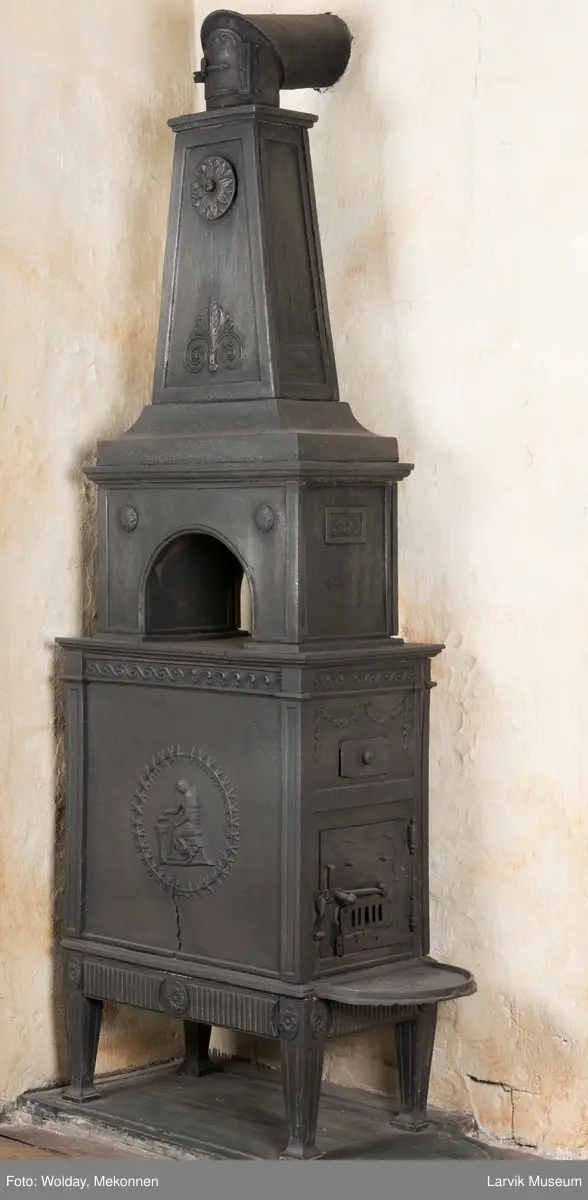 Tredelt , nederste etasje rektangulær fyrkasse/midtf.portalf/pyr.t. ben og sarg med kannelyrer og rosett i tre.  1.etasje langside: bladmedaljong, kvinne ved alter, øverst bølgemeander. 1.etasje kortside: bølgemeander, girlander og rosett 2.etasje langside: rundbuet åpning, i de øvre hjørner 2. etasje kortside: rosett i rektangel topp langside: palmett og rosett topp.Kortside: rosett i rektangel