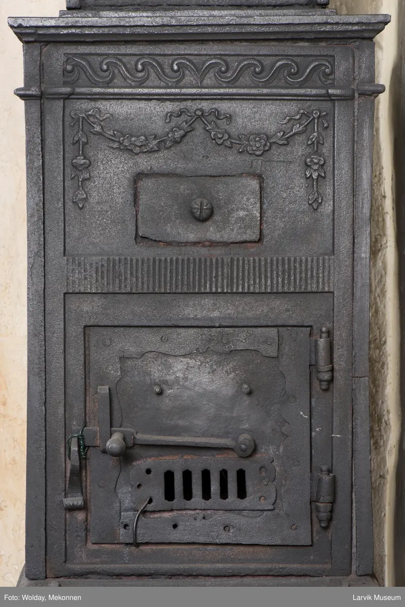 Tredelt , nederste etasje rektangulær fyrkasse/midtf.portalf/pyr.t. ben og sarg med kannelyrer og rosett i tre.  1.etasje langside: bladmedaljong, kvinne ved alter, øverst bølgemeander. 1.etasje kortside: bølgemeander, girlander og rosett 2.etasje langside: rundbuet åpning, i de øvre hjørner 2. etasje kortside: rosett i rektangel topp langside: palmett og rosett topp.Kortside: rosett i rektangel