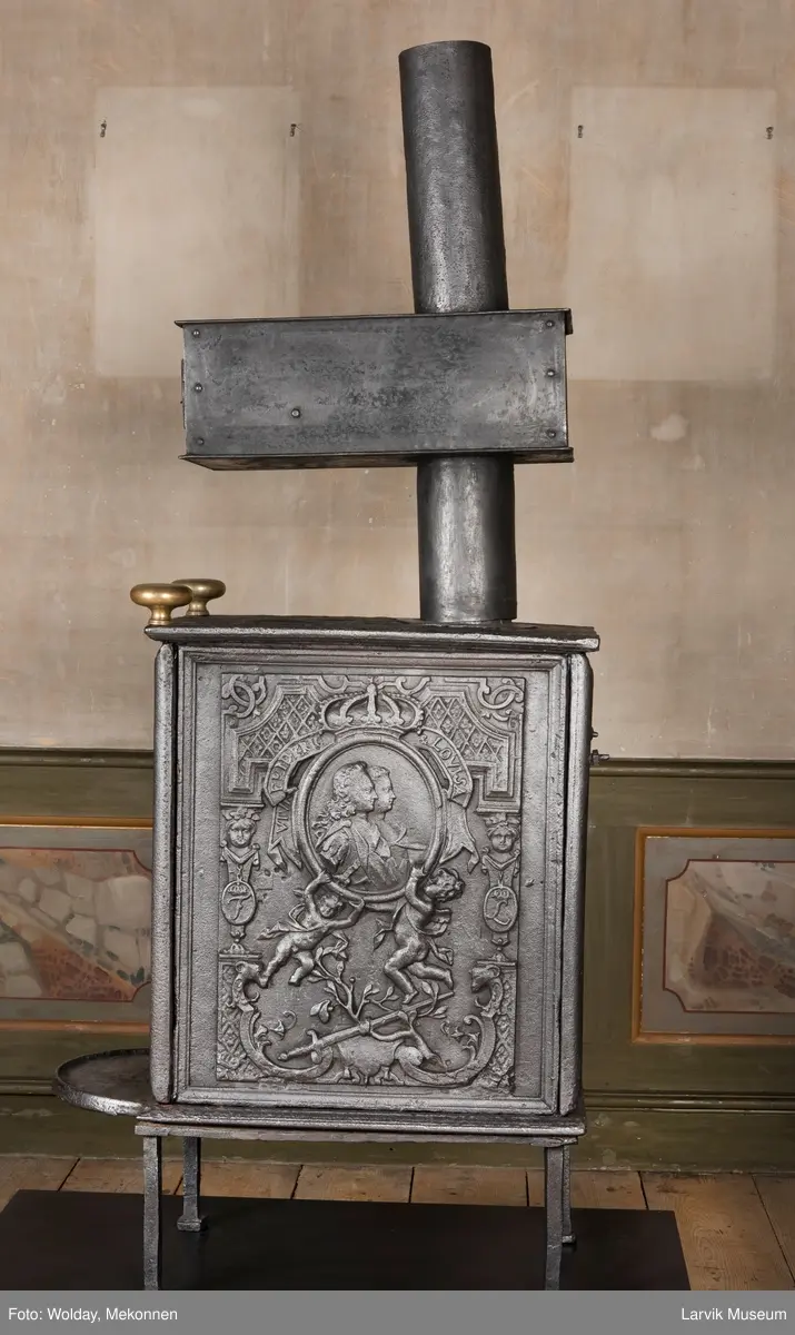 Ovnen har understell, bunnplate, sideplater, frontplate, bakplate og topp, røykkasse, røykerør og to messinghoder. Røykerøret er litt løst.