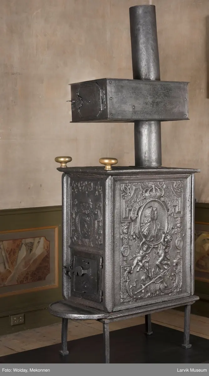 Ovnen har understell, bunnplate, sideplater, frontplate, bakplate og topp, røykkasse, røykerør og to messinghoder. Røykerøret er litt løst.