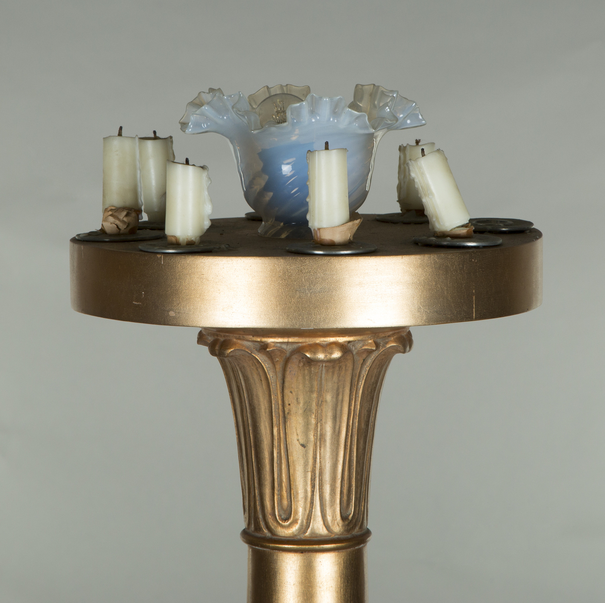 Forgylte gulvstående lamper for flere lys, både stearinlys og elektrisk. Hull til stearinlys langs kanten på hele topp-platen. En åpen lampeskjerm i glass omkranser det elektriske lyset midt på abakus, med bølgende kant (som en fakkel). Lampen er formet som en frittstående gresk søyle med base. Glatt utforming, med et område med bladutskjæringer like under midten, samt på kapitélet. Rund abakus og firkantet base.