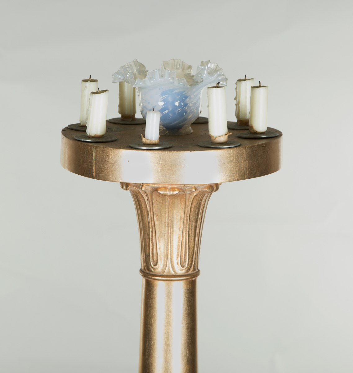 Forgylte gulvstående lamper for flere lys, både stearinlys og elektrisk. Hull til stearinlys langs kanten på hele topp-platen. En åpen lampeskjerm i glass omkranser det elektriske lyset midt på abakus, med bølgende kant (som en fakkel). Lampen er formet som en frittstående gresk søyle med base. Glatt utforming, med et område med bladutskjæringer like under midten, samt på kapitélet. Rund abakus og firkantet base. 
To av lampene har et forgylt tresylinder rundt pipen for det elektriske lyset. 
Var sannsynligvis ikke el.belysning originalt.