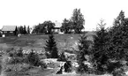 Skommarhyttans hyttruin i förgrunden. Huset på kullen hade Gammelstilla Bruk ställt till förfogande som skolhus innan skolan i Östansjö byggdes på 1880-talet.