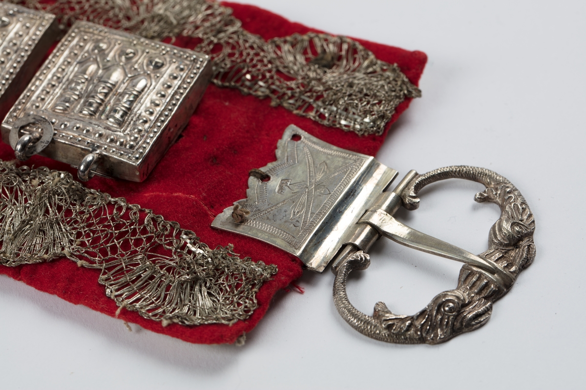 Rødt belte med sprette og sprot.
Stølar av sølv på rødt klede, sølvbeslag og metallknipling.