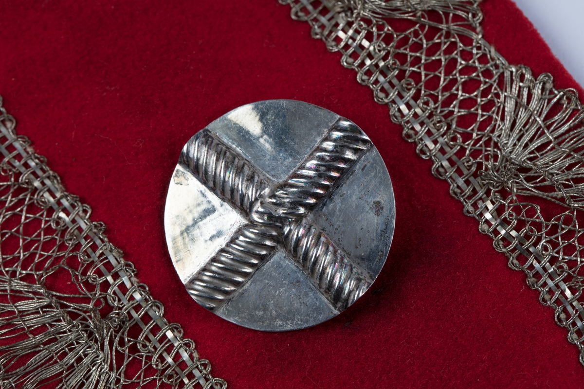 Rødt belte med sprette og sprot.
Stølar av sølv på rødt klede, sølvbeslag og metallknipling.