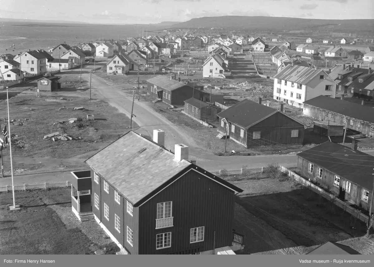 Vadsø 1957. Bilde tatt fra kirken mot vest. Prestegården er nærmest. Tverrgata er Fossevegen som ender i Damsveien. Veien mot vest finnes ikke lenger. I området foran ble Statens Hus senere bygget. Man ser brakker fra gjenreisingstida.