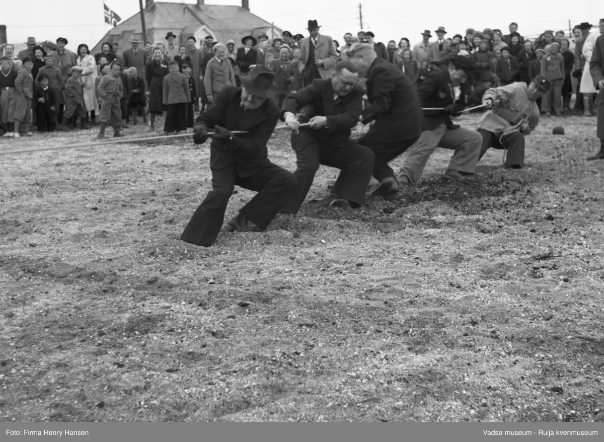 Vadsø 17 mai 1951. Tautrekkingskonkurranse. Vi ser "Skolens lag", fra venstre vaktmester Kristian Vara, lærer Karl Kristian Hoel lærer/folkeskolestyrer Rolf Skille og to ukjente. En stor menneskemengde, barn og voksne, står og bivåner det hele. 