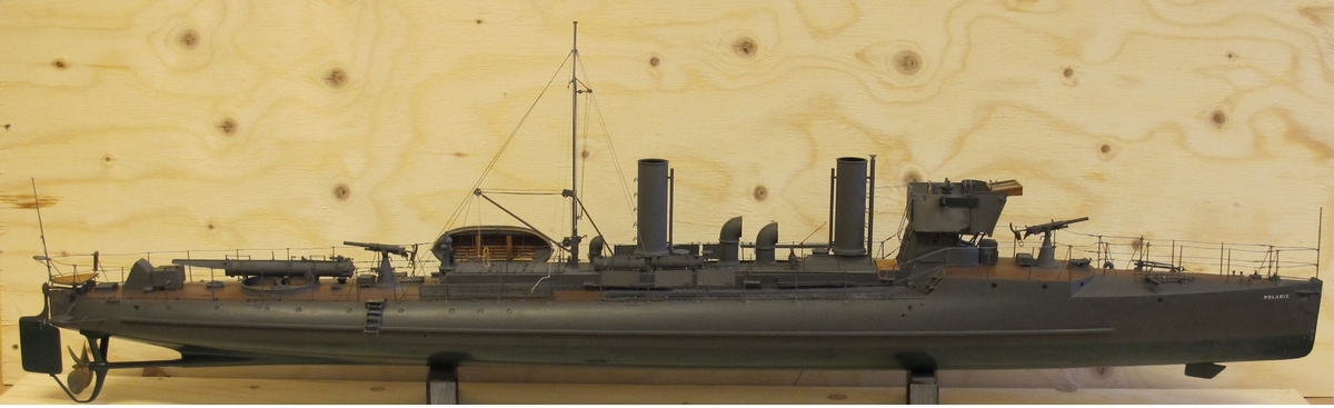 Fartygsmodell, lamelbyggd, fullständig däcksinredning, för- och akterroder, metallpropeller, däcks- och stävtub. 2 skorstenar, runda. Gråmålad, grön botten, korkfärgat däck. Riggad mast med vimpel, flaggspel med flagga, gösstake med gös. Fallrepstrappor. Julle, inredd, med roder och 2 ståvor. 2 st kanoner, gråmålade. Stativ 2 metallpelare. Tillverkad på statens bekostnad.