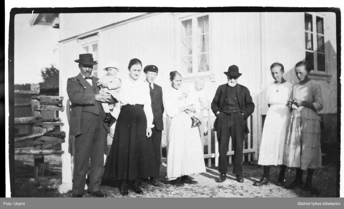 Gården Melleby i Tune. Personer fotografert foran huset på gården. 
Fra venstre: Aksel, Arne, Sofie, Olav Sørensen, Lovise, Solveig, Mathis, Marie, Anna Sørensen.
