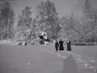 Tre personer står i snön utanför Tuna gård 1913.