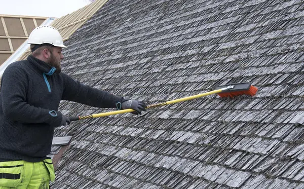Mann med hjelm står med kost og børster flistak.