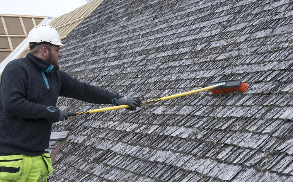 Mann med hjelm står med kost og børster flistak.