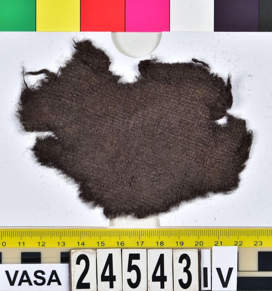 Textil.
Fyndnummer 24543 innehåller ca 381 textilfragment/textilföremål samt 8 träfragment uppdelade på 24543:I-VII.
Fnr 24543:I består av 175 fragment av ull vävda i 2/1-kypert. Tyget har fallit sönder i långa remsor. Kan det ha varit en filt, eller bara ett tygstycke? Varpen kan ha varit av vegetabiliska fibrer som brytits ner.
Fnr 24543:II är en filtad hatt. Hatten har rundad låg kulle. På kullens översida finns stukning i form av ett nyp. Hattens brätte är uppvikt och fäst vid kullen.
Fnr 24543:III består av 33 fragment av ull vävda i 2/1-kypert. Några av fragmenten har en bevarad originalkant med fåll eller söm med tråd kvar.
Fnr 24543:IV består av ett fragment av ull vävt i tuskaft. Tyget kan ha varit valkat.
Fnr 24543:V består av 35 fragment av ull vävda i tuskaft som varit en penningpung. 22 klippingar (20 st 1 öres samt 2 st 1/2 öres) återfanns tillsammans med tyget. Tyget har svartgröna märken efter myntens kanter. Några av de mindre fragmenten är korrosionsflagor, inte tyg. Pungen måste ha legat nära järn för den är orange av korrosion. Pungens tyg är i nuläget dubbelvikt (utfläkt) så att insidan syns på båda sidorna av fragmentet. i övre kantens insida sitter en hårtuss fast (ull eller vad?). Några av fragmenten har några originalkanter kvar.
Fnr 24543:VI är 8 stycken tunna små träfragment.
Fnr 24543:VI a består av ca 60 fragment av ull vävda i tuskaft. Kan ha varit en jacka. Många av fragmenten har bevarade originalkanter med fållar och sömmar med tråd kvar. På ett tygstycke som är höger framhalva syns 9 hål som varit snörda med ett smalt band, varav en liten bit fortfarande finns kvar genom två av hålen. 
Fnr 24543:VI a:2 består av 58 fragment av ull vävda i tuskaft. Några av fragmenten har originalkanter med spår av söm kvar.
Fnr 24543:VI b består av 15 fragment av ull vävda i 2/1-kypert. 
Fnr 24543:VII består av 2 slätstickade fragment av ull. Recenta? Ser maskinstickade ut." 
Fnr 24543: ett fragment av ull vävt i tuskaft som inte hade någon romersk siffra på sig men som låg tillsammans med de andra fragmenten från detta fyndnummer och därför mest troligen också hör dit även om det inte står till vilket lager det hört. Tyget kan ha varit valkat på ena sidan. Fragmentet har 2 originalkanter med spår av sömmar.