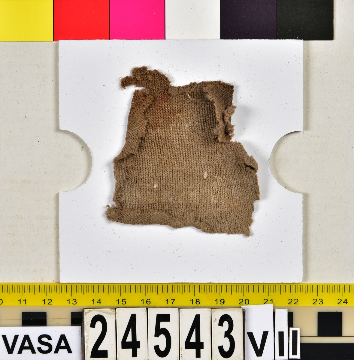 Textil.
Fyndnummer 24543 innehåller ca 381 textilfragment/textilföremål samt 8 träfragment uppdelade på 24543:I-VII.
Fnr 24543:I består av 175 fragment av ull vävda i 2/1-kypert. Tyget har fallit sönder i långa remsor. Kan det ha varit en filt, eller bara ett tygstycke? Varpen kan ha varit av vegetabiliska fibrer som brytits ner.
Fnr 24543:II är en filtad hatt. Hatten har rundad låg kulle. På kullens översida finns stukning i form av ett nyp. Hattens brätte är uppvikt och fäst vid kullen.
Fnr 24543:III består av 33 fragment av ull vävda i 2/1-kypert. Några av fragmenten har en bevarad originalkant med fåll eller söm med tråd kvar.
Fnr 24543:IV består av ett fragment av ull vävt i tuskaft. Tyget kan ha varit valkat.
Fnr 24543:V består av 35 fragment av ull vävda i tuskaft som varit en penningpung. 22 klippingar (20 st 1 öres samt 2 st 1/2 öres) återfanns tillsammans med tyget. Tyget har svartgröna märken efter myntens kanter. Några av de mindre fragmenten är korrosionsflagor, inte tyg. Pungen måste ha legat nära järn för den är orange av korrosion. Pungens tyg är i nuläget dubbelvikt (utfläkt) så att insidan syns på båda sidorna av fragmentet. i övre kantens insida sitter en hårtuss fast (ull eller vad?). Några av fragmenten har några originalkanter kvar.
Fnr 24543:VI är 8 stycken tunna små träfragment.
Fnr 24543:VI a består av ca 60 fragment av ull vävda i tuskaft. Kan ha varit en jacka. Många av fragmenten har bevarade originalkanter med fållar och sömmar med tråd kvar. På ett tygstycke som är höger framhalva syns 9 hål som varit snörda med ett smalt band, varav en liten bit fortfarande finns kvar genom två av hålen. 
Fnr 24543:VI a:2 består av 58 fragment av ull vävda i tuskaft. Några av fragmenten har originalkanter med spår av söm kvar.
Fnr 24543:VI b består av 15 fragment av ull vävda i 2/1-kypert. 
Fnr 24543:VII består av 2 slätstickade fragment av ull. Recenta? Ser maskinstickade ut." 
Fnr 24543: ett fragment av ull vävt i tuskaft som inte hade någon romersk siffra på sig men som låg tillsammans med de andra fragmenten från detta fyndnummer och därför mest troligen också hör dit även om det inte står till vilket lager det hört. Tyget kan ha varit valkat på ena sidan. Fragmentet har 2 originalkanter med spår av sömmar.