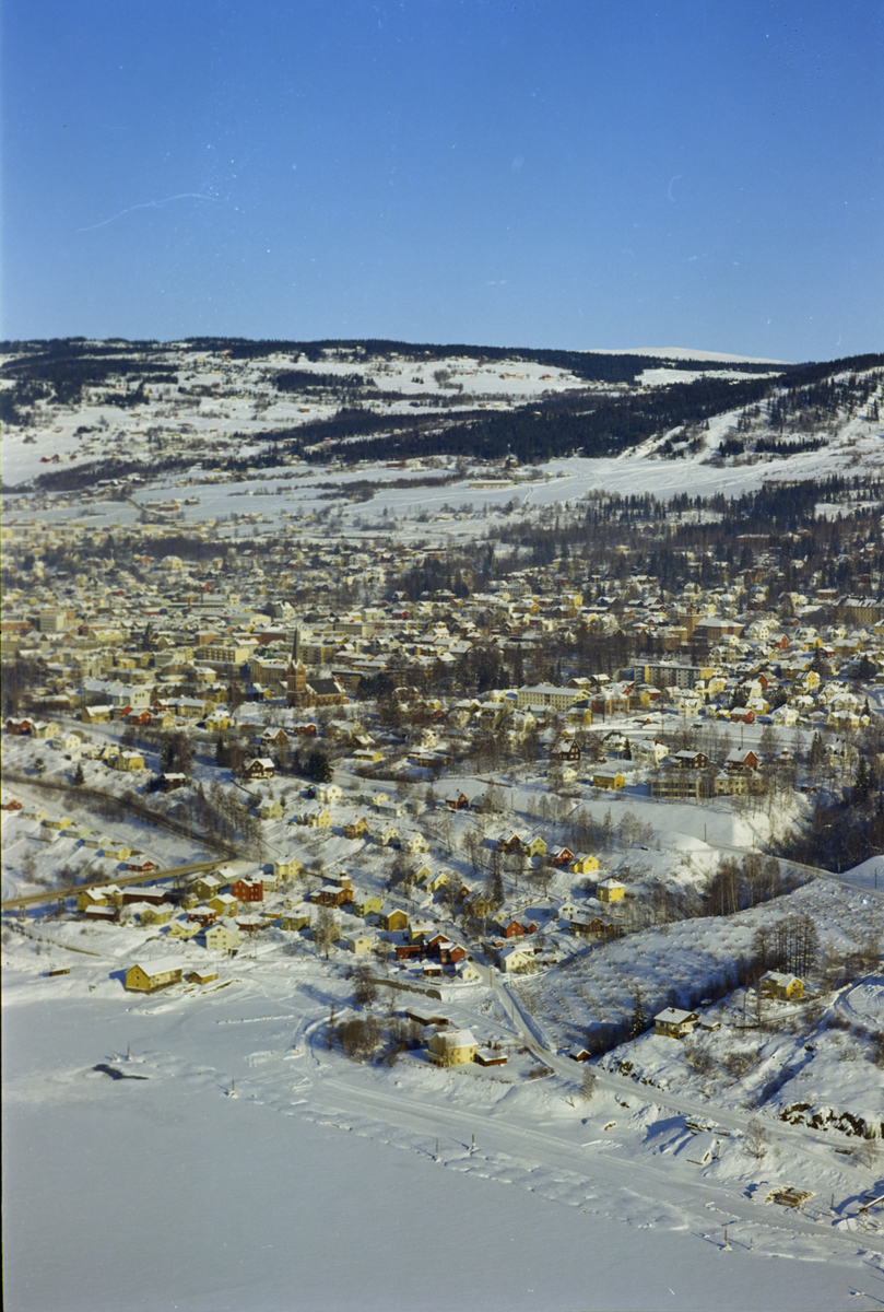 Lillehammer, oversiktsbilde, vinter. Bygninger med Lillehammer Kirke sees midt på bildet, til høyre for den, Sportsplassen som er islagt for skøyting. Nederst Thorstadbua ved Mjøsa og øverst på bildet Lysgård med jorder omkring.