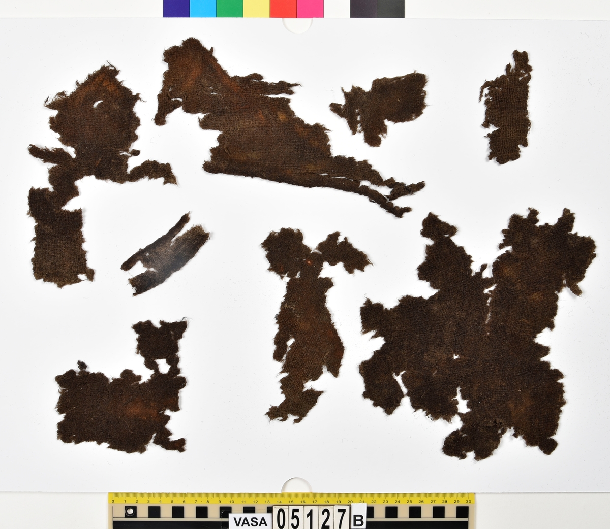 Textil.
Fyndnummer 05127 är uppdelat i a-e.
Fnr 05127a består av 9 fragment av ull vävda i 2/2-kypert. 
Fnr 05127b består av 8 fragment av ull vävda i tuskaft. Tyget är mer valkat på ena sidan än den andra. Två av fragmenten har delar av originalkanter, med spår av sömmar, kvar.
Fnr 05127c består av 4 fragment av ull vävda i tuskaft. Alla fragmenten har delar av originalkanter, med spår av sömmar, kvar.
Fnr 05127d består av ett fragment av ull vävt i tuskaft. Fragmentet en originalkant, med spår av söm, kvar.
Fnr 05127e består av 3 fragment av ull vävda i gles tuskaft.