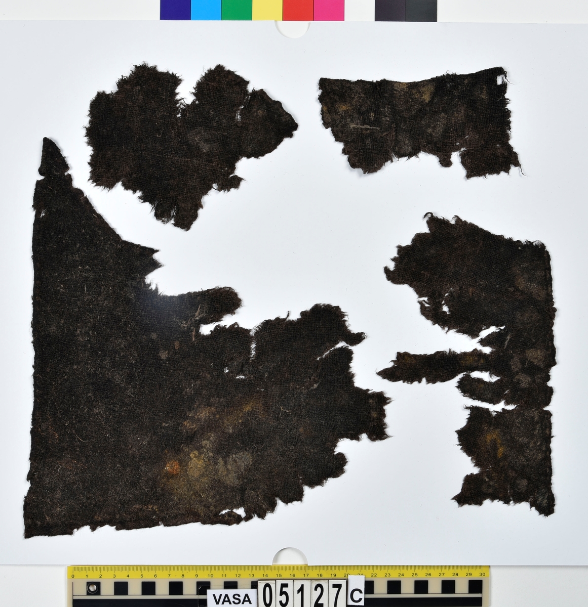Textil.
Fyndnummer 05127 är uppdelat i a-e.
Fnr 05127a består av 9 fragment av ull vävda i 2/2-kypert. 
Fnr 05127b består av 8 fragment av ull vävda i tuskaft. Tyget är mer valkat på ena sidan än den andra. Två av fragmenten har delar av originalkanter, med spår av sömmar, kvar.
Fnr 05127c består av 4 fragment av ull vävda i tuskaft. Alla fragmenten har delar av originalkanter, med spår av sömmar, kvar.
Fnr 05127d består av ett fragment av ull vävt i tuskaft. Fragmentet en originalkant, med spår av söm, kvar.
Fnr 05127e består av 3 fragment av ull vävda i gles tuskaft.