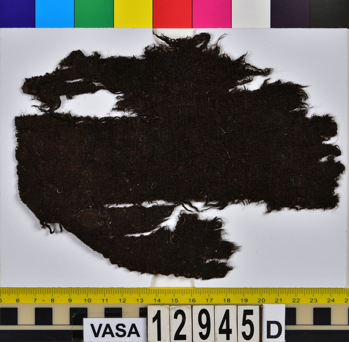 Textilfragment.
15 textilfragment uppdelade på fyndnummer 12945a-g.
Fnr 12945a består av fyra fragment av ull vävda i tuskaft. Två av fragmenten har rester av söm eller fåll samt har varit valkade.
Fnr 12945b består av två fragment av ull vävda i tuskaft. 
Fnr 12945c består av ett fragment av ull vävt i tuskaft. Fragmentet kan ha varit valkat på ena sidan.
Fnr 12945d består av ett fragment av ull vävt i tuskaft. Fragmentet har en söm med rester av stygn kvar i ena kanten.
Fnr 12945e består av tre fragment av ull vävda i tuskaft. Fragmentet har en tydlig originalkant bevarad.
Fnr 12945f består av ett filtat fragment. Kan möjligen ha varit en del av ett hattbrätte.
Fnr 12945g består av tre filtade fragment, troligen av ull.