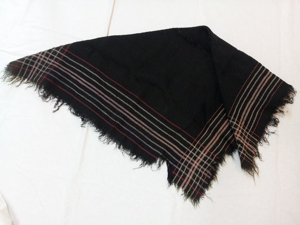 Kvadratisk tørkle/sjal. Vove i svart ull med stripemønster langs kantane. På to langsider kvite og oransje striper, på dei to andre langsidene kvite og lilla striper. Korte frynser. Laust vove.