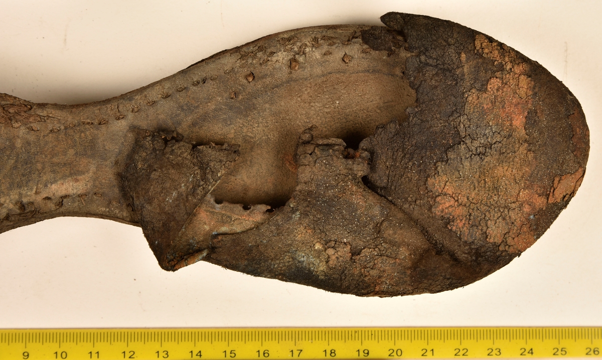 Dokumentation 1996:
Delar och fragment av sko: en skobotten samt ett fragmentariskt ovanläder, tre bitar av ett filtliknande material, ett 15-tal fragment av bottenläder samt sex mindre fragment av trä.
Skobottnen har kvarsittande tråd och träpligg. Yttersulan är ritsad. Klacken består av fem klacklappar som är placerade mellan ytter- och innersulan. Innersulans läder är mycket kraftigt, ca 6 mm tjock. Ovanlädret är sprött och fragmentariskt samt har blå och rostfärgade utfällningar.

Text in English: 
Various parts and fragments of a shoe, consisting of a sole with fragments of vamp (upper leather), three pieces of a felt-like material, some 15 fragments of sole or bottom leather and six smaller fragments of wood.
There are remains of thread and wooden pegs on the shoe sole. The outsole is channeled. The heel is made up of five heel lifts placed between the insole and outsole. The leather of the insole is very thick, ca 6 mm. The upper leather is fragile and fragmentary, and has blue and rust-coloured precipitations.

Dokumentation 2022:
Skobotten och delar av ovanläder till en öppen randsko. Tillverkade i getskinn av god kvalitet. Skapades på en rak läst och bars på höger fot. Klacken som är lagad med en läderlapp under sulan. Inga dekorationer. Det finns tecken på delaminering. Fragment från en stickad strumpa hittades inuti skon. Det finns lagningar med träpligg på sulan och hälen. Skobotten hör ihop med fyndnummer 23070.
För mer information, se Länkade filer: Uppritning

Text in english:
This is the bottom unit and upper fragments of an open shoe, made of goatskin leather of good quality, of randed construction with a patch heel, made on a straight last and worn on the right foot, with no decorative features. The bottom unit pairs with 23070. There are signs of delamination and fragments of a knitted stocking were found inside the shoe. There are pegged repairs to sole and heel.
For more information, go to Länkade filer: Uppritning