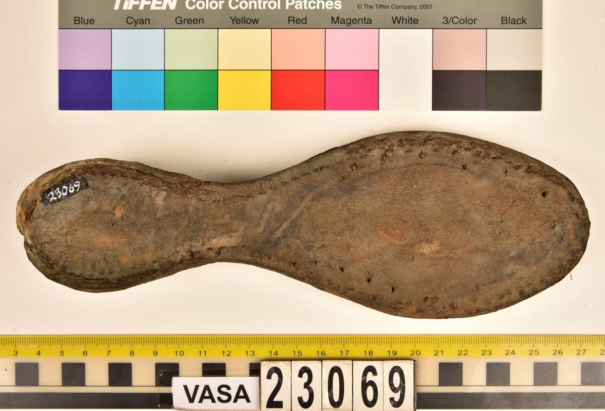 Dokumentation 1996:
Delar och fragment av sko: en skobotten samt ett fragmentariskt ovanläder, tre bitar av ett filtliknande material, ett 15-tal fragment av bottenläder samt sex mindre fragment av trä.
Skobottnen har kvarsittande tråd och träpligg. Yttersulan är ritsad. Klacken består av fem klacklappar som är placerade mellan ytter- och innersulan. Innersulans läder är mycket kraftigt, ca 6 mm tjock. Ovanlädret är sprött och fragmentariskt samt har blå och rostfärgade utfällningar.

Text in English: 
Various parts and fragments of a shoe, consisting of a sole with fragments of vamp (upper leather), three pieces of a felt-like material, some 15 fragments of sole or bottom leather and six smaller fragments of wood.
There are remains of thread and wooden pegs on the shoe sole. The outsole is channeled. The heel is made up of five heel lifts placed between the insole and outsole. The leather of the insole is very thick, ca 6 mm. The upper leather is fragile and fragmentary, and has blue and rust-coloured precipitations.

Dokumentation 2022:
Skobotten och delar av ovanläder till en öppen randsko. Tillverkade i getskinn av god kvalitet. Skapades på en rak läst och bars på höger fot. Klacken som är lagad med en läderlapp under sulan. Inga dekorationer. Det finns tecken på delaminering. Fragment från en stickad strumpa hittades inuti skon. Det finns lagningar med träpligg på sulan och hälen. Skobotten hör ihop med fyndnummer 23070.
För mer information, se Länkade filer: Uppritning

Text in english:
This is the bottom unit and upper fragments of an open shoe, made of goatskin leather of good quality, of randed construction with a patch heel, made on a straight last and worn on the right foot, with no decorative features. The bottom unit pairs with 23070. There are signs of delamination and fragments of a knitted stocking were found inside the shoe. There are pegged repairs to sole and heel.
For more information, go to Länkade filer: Uppritning