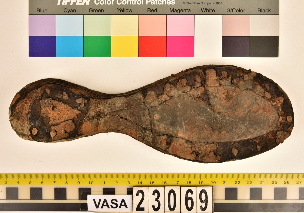 Dokumentation 1996:
Delar och fragment av sko: en skobotten samt ett fragmentariskt ovanläder, tre bitar av ett filtliknande material, ett 15-tal fragment av bottenläder samt sex mindre fragment av trä.
Skobottnen har kvarsittande tråd och träpligg. Yttersulan är ritsad. Klacken består av fem klacklappar som är placerade mellan ytter- och innersulan. Innersulans läder är mycket kraftigt, ca 6 mm tjock. Ovanlädret är sprött och fragmentariskt samt har blå och rostfärgade utfällningar.

Text in English: 
Various parts and fragments of a shoe, consisting of a sole with fragments of vamp (upper leather), three pieces of a felt-like material, some 15 fragments of sole or bottom leather and six smaller fragments of wood.
There are remains of thread and wooden pegs on the shoe sole. The outsole is channeled. The heel is made up of five heel lifts placed between the insole and outsole. The leather of the insole is very thick, ca 6 mm. The upper leather is fragile and fragmentary, and has blue and rust-coloured precipitations.

Dokumentation 2022:
Skobotten och delar av ovanläder till en öppen randsko. Tillverkade i getskinn av god kvalitet. Skapades på en rak läst och bars på höger fot. Klacken som är lagad med en läderlapp under sulan. Inga dekorationer. Det finns tecken på delaminering. Fragment från en stickad strumpa hittades inuti skon. Det finns lagningar med träpligg på sulan och hälen. Skobotten hör ihop med fyndnummer 23070.
För mer information, se Länkade filer: Uppritning

Text in english:
This is the bottom unit and upper fragments of an open shoe, made of goatskin leather of good quality, of randed construction with a patch heel, made on a straight last and worn on the right foot, with no decorative features. The bottom unit pairs with 23070. There are signs of delamination and fragments of a knitted stocking were found inside the shoe. There are pegged repairs to sole and heel.
For more information, go to Länkade filer: Uppritning