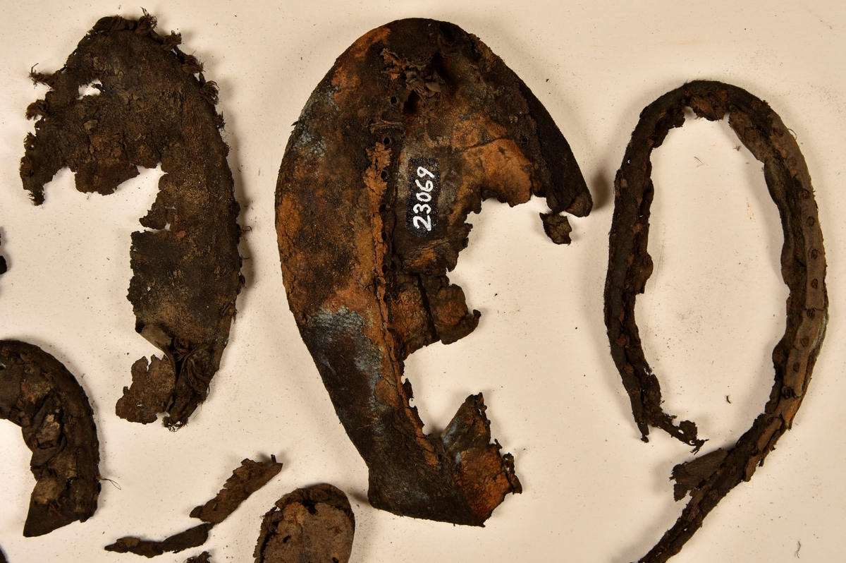 Dokumentation 1996:
Delar och fragment av sko: en skobotten samt ett fragmentariskt ovanläder, tre bitar av ett filtliknande material, ett 15-tal fragment av bottenläder samt sex mindre fragment av trä.
Skobottnen har kvarsittande tråd och träpligg. Yttersulan är ritsad. Klacken består av fem klacklappar som är placerade mellan ytter- och innersulan. Innersulans läder är mycket kraftigt, ca 6 mm tjock. Ovanlädret är sprött och fragmentariskt samt har blå och rostfärgade utfällningar.

Text in English: 
Various parts and fragments of a shoe, consisting of a sole with fragments of vamp (upper leather), three pieces of a felt-like material, some 15 fragments of sole or bottom leather and six smaller fragments of wood.
There are remains of thread and wooden pegs on the shoe sole. The outsole is channeled. The heel is made up of five heel lifts placed between the insole and outsole. The leather of the insole is very thick, ca 6 mm. The upper leather is fragile and fragmentary, and has blue and rust-coloured precipitations.

Dokumentation 2022:
Skobotten och delar av ovanläder till en öppen randsko. Tillverkade i getskinn av god kvalitet. Skapades på en rak läst och bars på höger fot. Klacken som är lagad med en läderlapp under sulan. Inga dekorationer. Det finns tecken på delaminering. Fragment från en stickad strumpa hittades inuti skon. Det finns lagningar med träpligg på sulan och hälen. Skobotten hör ihop med fyndnummer 23070.
För mer information, se Länkade filer: Uppritning

Text in english:
This is the bottom unit and upper fragments of an open shoe, made of goatskin leather of good quality, of randed construction with a patch heel, made on a straight last and worn on the right foot, with no decorative features. The bottom unit pairs with 23070. There are signs of delamination and fragments of a knitted stocking were found inside the shoe. There are pegged repairs to sole and heel.
For more information, go to Länkade filer: Uppritning
