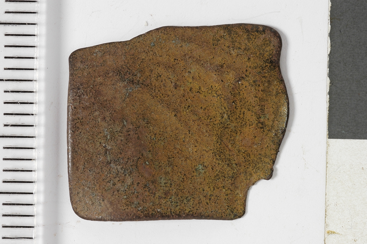 En ujevn metallplate med  kvadratliknende form og to bruddflater. Dette kan være et plateavklipp fra metallhåndverk.