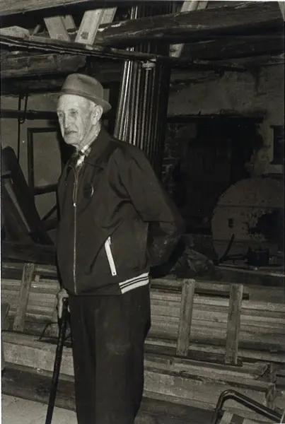 Kælkkjøreren Kristian Berntsen. Tatt inne i fabrikken etter at han ble pensjonist. Står med stokk og hatt.