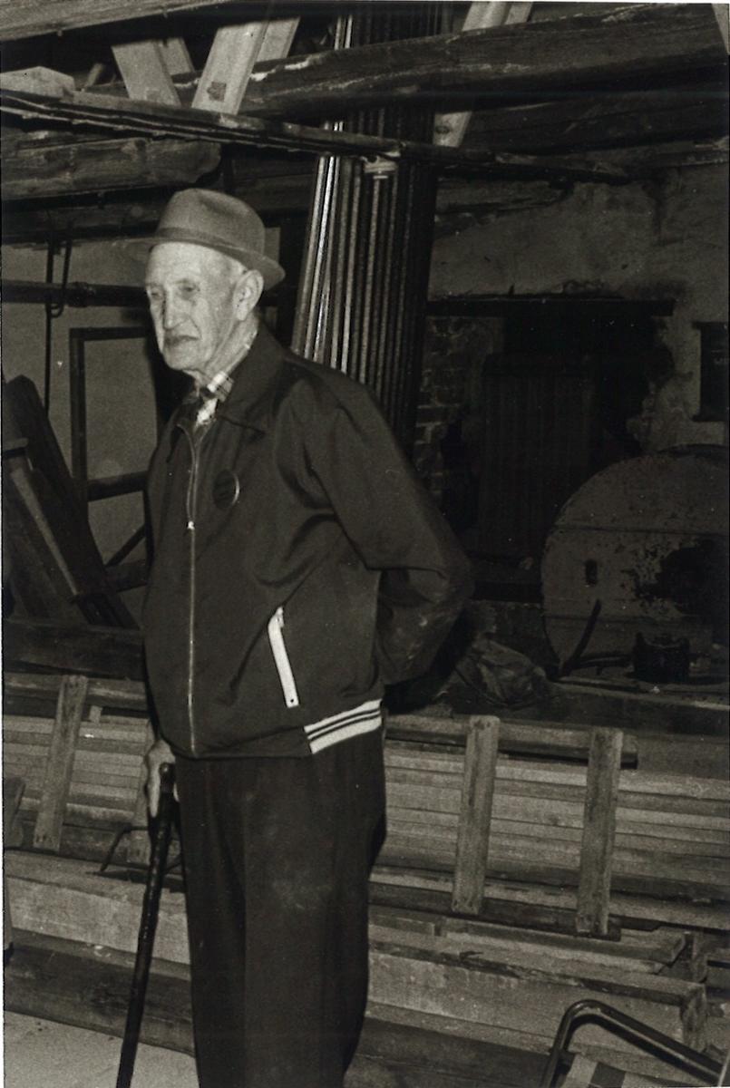 Kælkkjøreren Kristian Berntsen. Tatt inne i fabrikken etter at han ble pensjonist. Står med stokk og hatt.