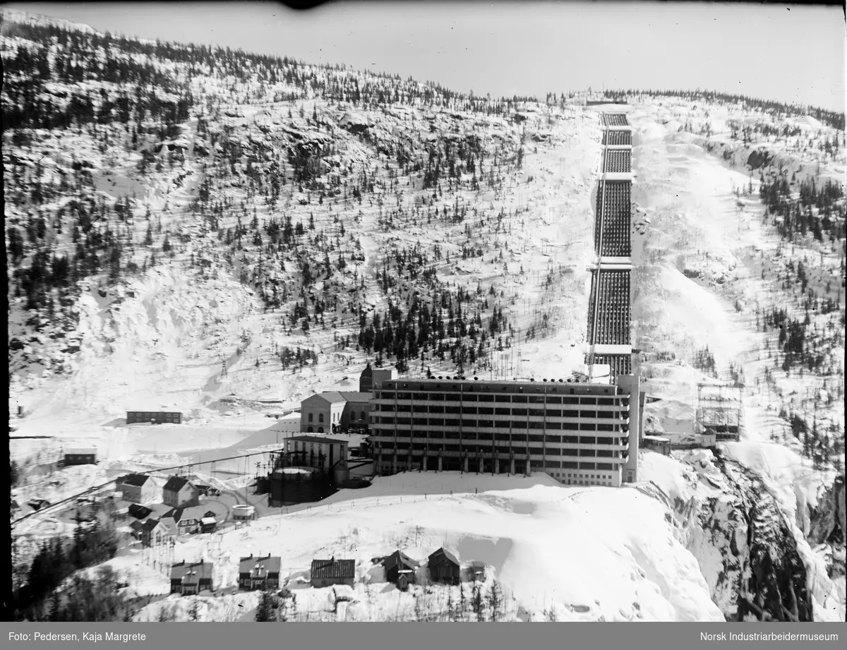 Hydrogenfabrikken Vemork (vannstoffen) med rørgaten til Vemork Kraftstasjon i bakgrunnen. Bolighus foran fabrikken.