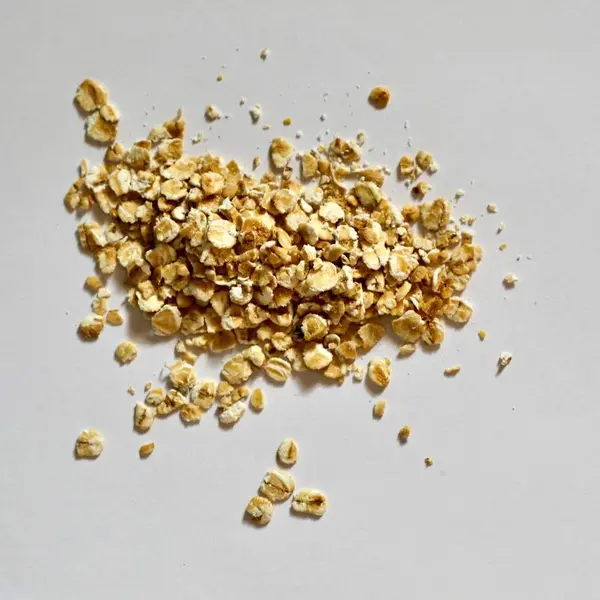 Havregryn er flattrykte havrekorn med litt varierende lys beige farge, her ligger det i en haug på et grått underlag.