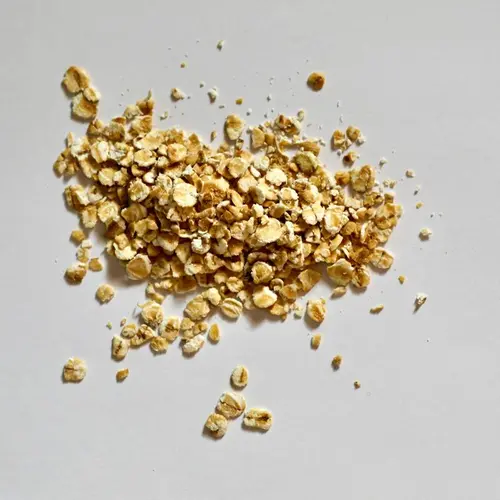 Havregryn er flattrykte havrekorn med litt varierende lys beige farge, her ligger det i en haug på et grått underlag.