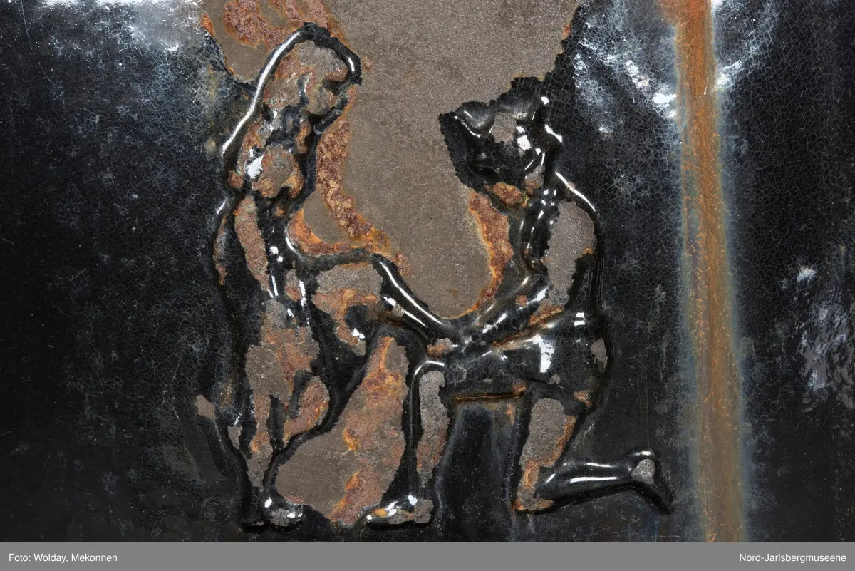 Relieffer: 1. på fronten: Askepott og prinsen som prøver om skoen passer. 2. På sidene: Askepott i grua med slottet i bakgrunnen. På grindene på dobbeltdørene til kokerom: en medaljong med grytemotiv, grinden med gjennombrutt labyrintmønster.