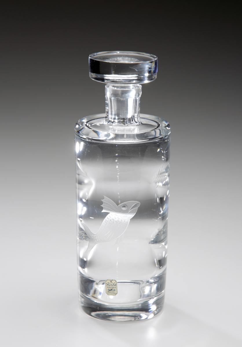 Karaff formgiven av Elis Bergh.
Se även snapsglas M 15159:a-f.
Ringoptik.
Halsen slipad i åtta facetter. Graverad fisk. Slipad propp. 
Ofärgat klarglas.
Ovan angivna mått avser höjd med propp.
Inskriven i huvudkatalogen 1959.
Funktion: Karaff