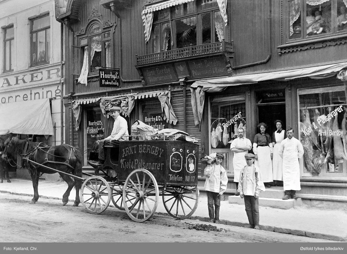 Arnt Bergbys slakterforretning i St. Mariegate i Sarpsborg ca. 1913-14. Til venstre Haarby & Co. Fiskeutsalg. (Innehaver Karl Ludvig Haarby f. 1967, sersjant og fiskehandler).

I andre etasje i vinduet: Olga Bergby med Solveig på armen, Aslaug til venstre i bildet, så Arne og Haakon. Arnt Bergby kjører vogna. 
På trappa: til venstre Axel Nilsen, Marie Bergby (søster)Bertelsen, Ludvig Ludvigsen. 
Guttene foran, en av dem ble kalt Harald Solid (ble kalt for  "Solingen" Mannen bak vogna er ukjent.
Reklame: Arnt Bergby Kjøt & Pølser Slakteforretning Pølsemakeri & Røkeri. Linselus i vinduet øverst til høyre.