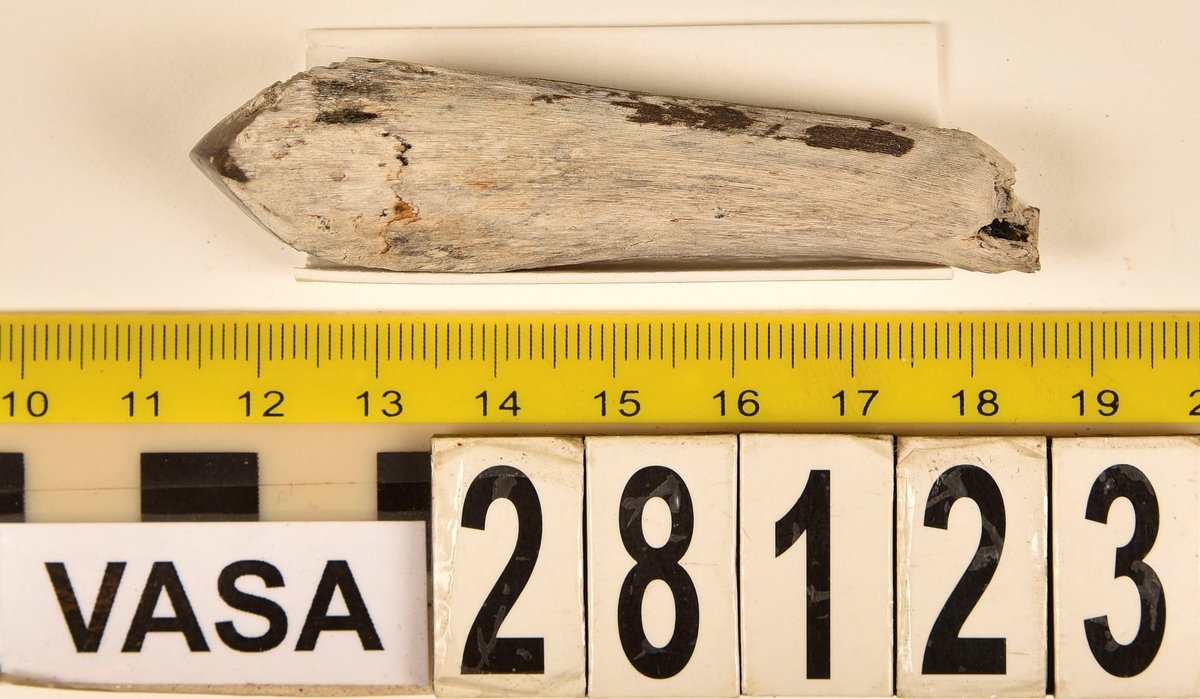 Fragment av horn. Avbruten i ena änden och sågad diagonalt till en spets i den andra änden. Ena sågytan har slipad sida. Hornets ursprungliga yta är bortnött och ytan känns närmast som torkat trä.