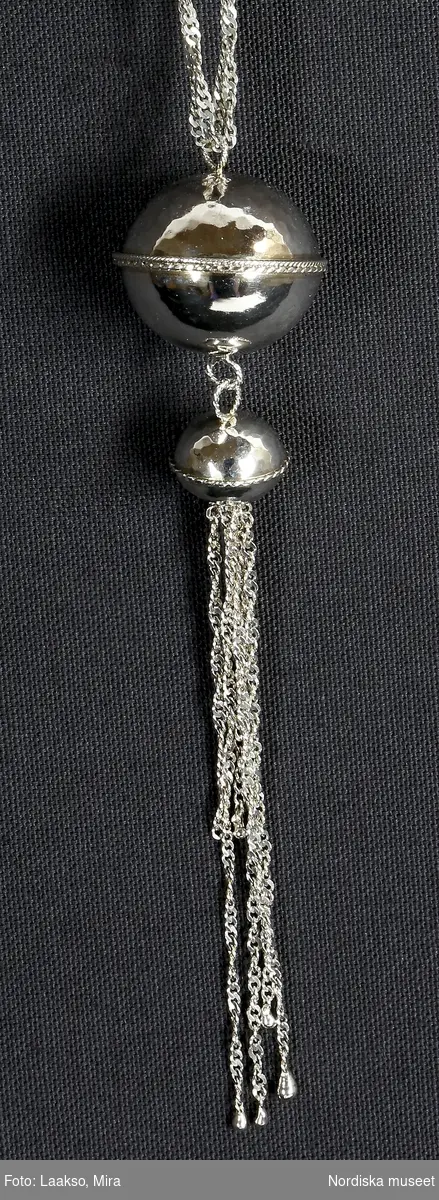 Hängsmycke av silver, "Moder jord" 925/2000, på dubbel silverkedja av platta länkar, spiralformad. Hängsmycket bestående av ett större och ett mindre klot, sammansatta med öglor av tvinnad silvertråd, det större klotet överst. Det mindre klotet avslutas nedåt med sex löst hängande kedjor av olika längd, spiralformade av samma slag som halskedjan.

Graverad på den större silverkulans nedre halva är Rosa Taikons signatur, samt silverstämplar.
/Helena Lindroth & Petrine Knight, 2014-02-18
