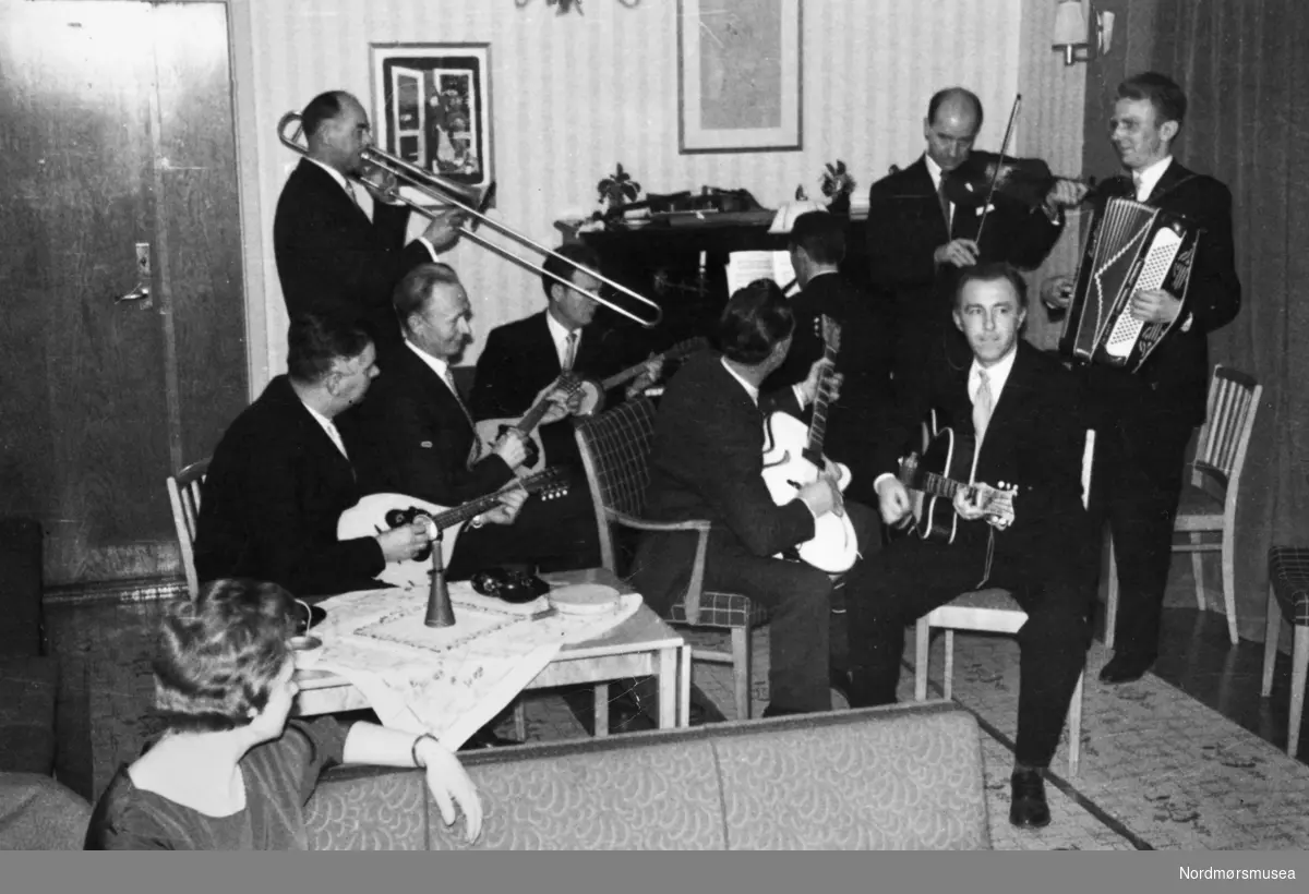 Musikervennene «Jularbos Venner», holder årsfest med ektefeller i Odd Fellows lokaler, januar 1959. Fra venstre første rekke: Nils Rødahl, mandolin, Johan Aasen, mandolin, Helge Eilertsen, gitar, Johan Tømmervåg, gitar. Bakerste rekke: Bjarne Sakshaug, trombone, Oddvar Grytli, banjo, Reidar Sylthe, piano, Bjarne Teiseth, fiolin, Gunnar Tømmervåg, trekkspill. Nærmest fotografen: ukjent. Originalfotoet er i Gunnar Tømmervågs eie. Fra Nordmøre museums fotosamlinger.