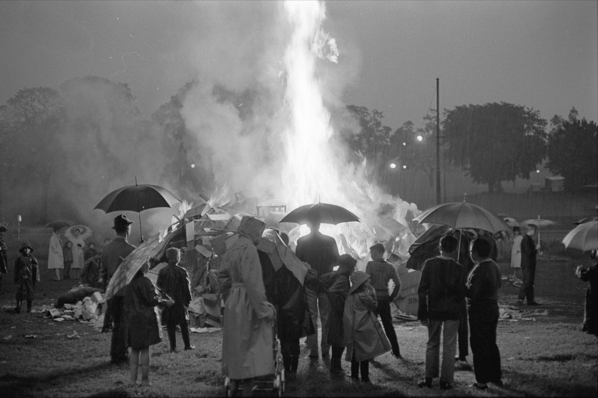 Norge, 23.06.1964. St. Hans feiring. Bål og mennesker med paraplyer.