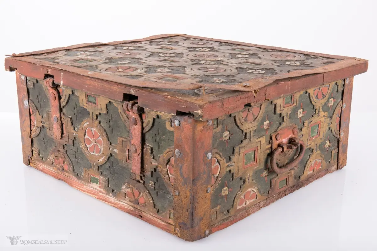 Skårede røde blomster med sirkulær innramming og grønne kvadrater med kvadratisk innramming som går i hverandre og går igjen på lokket. Innemellom disse figurene; små seksbladede hvite blomster med rød knapp. På sidene; grønne rektangler med innramming som går over i de samme røde blomstene med ramme som på lokket, men de fleste grenser mot kantene og blir halvmåneformede.