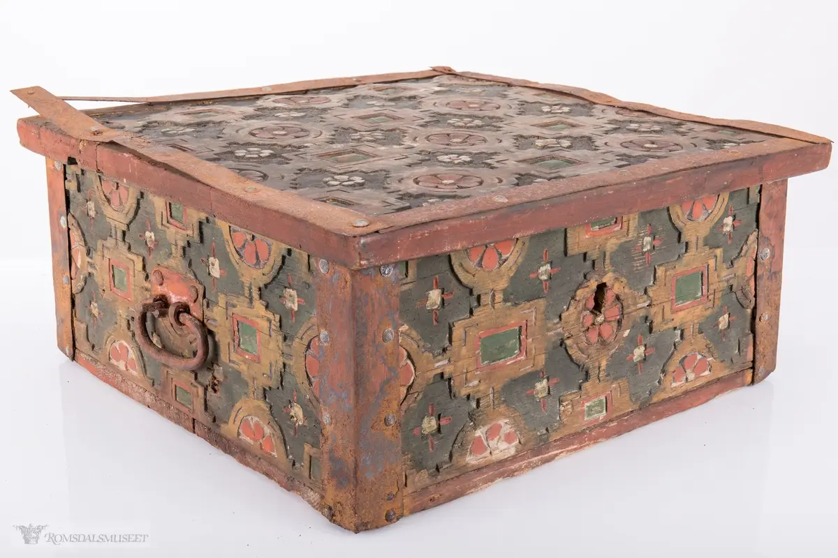 Skårede røde blomster med sirkulær innramming og grønne kvadrater med kvadratisk innramming som går i hverandre og går igjen på lokket. Innemellom disse figurene; små seksbladede hvite blomster med rød knapp. På sidene; grønne rektangler med innramming som går over i de samme røde blomstene med ramme som på lokket, men de fleste grenser mot kantene og blir halvmåneformede.