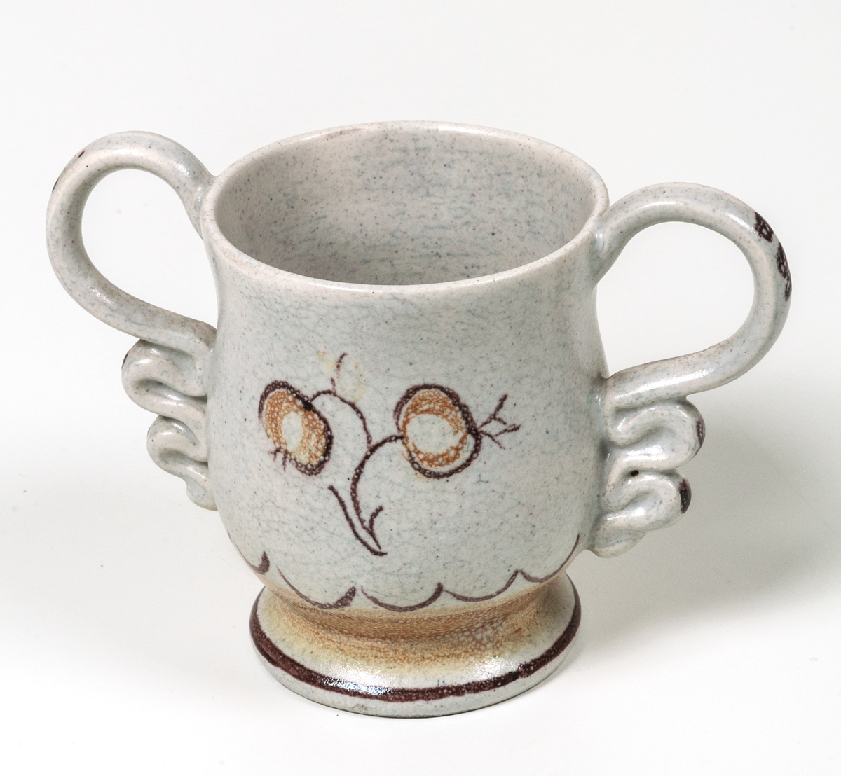 Bägare av lergods. Bo Fajans, design Eva Jancke­Björk. Grå S­svängd med stora hänklar, ljus- och mörkbruna partier nedtill samt dekor av en blomma.