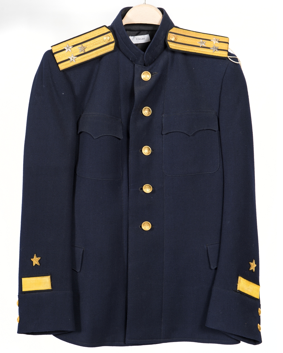 Kolett från ryska marinen för kapten av första rangen. Blått kläde. Fodrad med svart siden, i ärmarna vitt siden. Knäppt med 5 gulmetallknappar. 2 bröstfickor med lock och 2 höftfickor med lock. 1 ficka på var sida i fodret. 2 gulmetallknappar på var ärm. 1 guldstickat sterck och 1 guldstickad stjärna på var ärm. Axelklaffar med 3 längsgående guldgaloner mellan dessa svart silke, knapp i gulmetall 3 stjärnor i vitmetall.