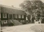 Harry Nilssons gård. Manbyggningen. Hög undervåning med kök m.m. Till vänster fritrappa upp till bostadesvåningen, rikt smitt räcke med APS.  Brutet tak. Tydligen byggd under 1800-talets förra del.