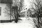 Ett bostadshus med putsad fasad och ett annat bostadshus med träfasad och veranda under vintertid. En cykel finns också med på bilden.