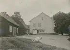 Till höger huvudbyggnaden. Närmast denna en bobyggnad av timmer i stolpar, brutet tak.