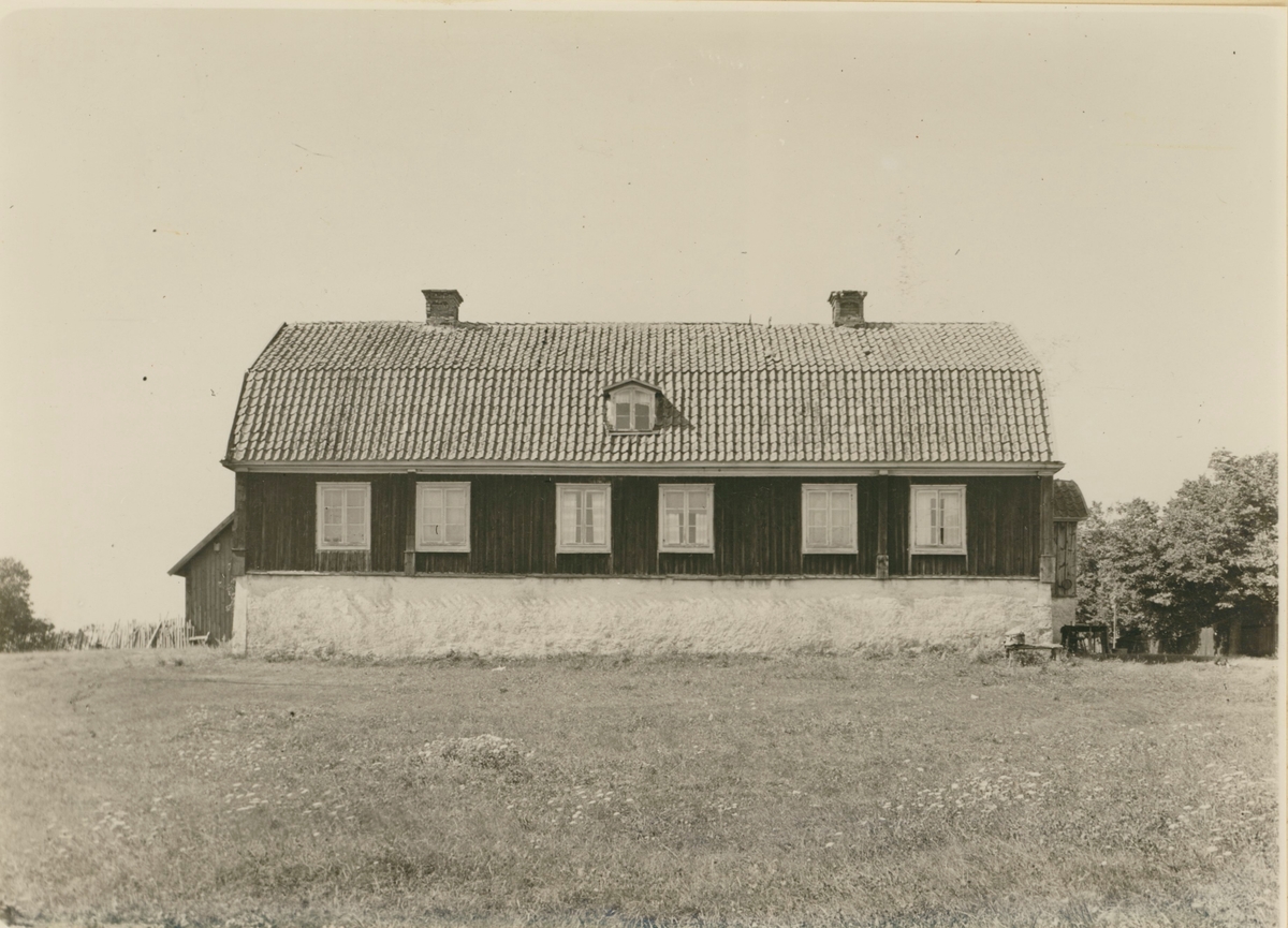 Huvudbyggningen. Av timmer på hög stenfot. Väggarna tjärade. Rikt utformad taklist.